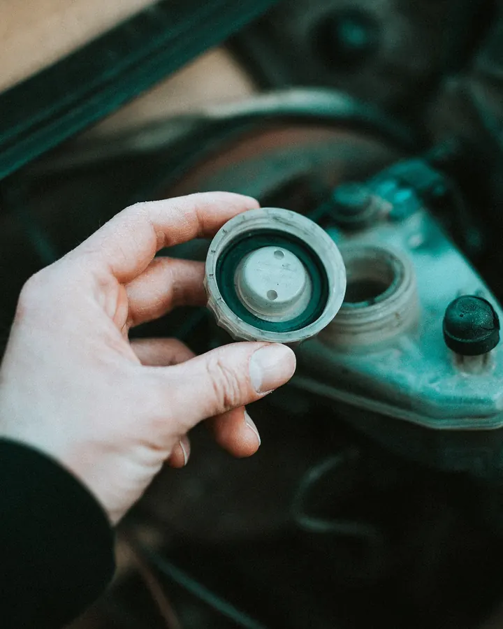 A hand lifting the cap of a fluid reservoir in an engine bay