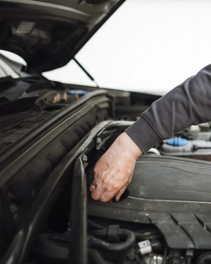 A mechanic’s arms reaching into the engine bay of a car