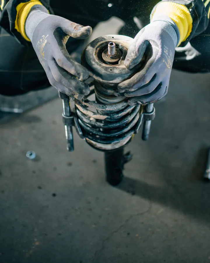 Gloved hands holding a suspension strut with its coil spring